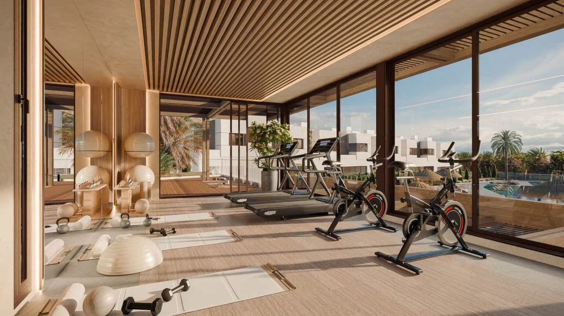 Modern indoor gym with floor-to-ceiling windows overlooking a swimming pool and palm trees